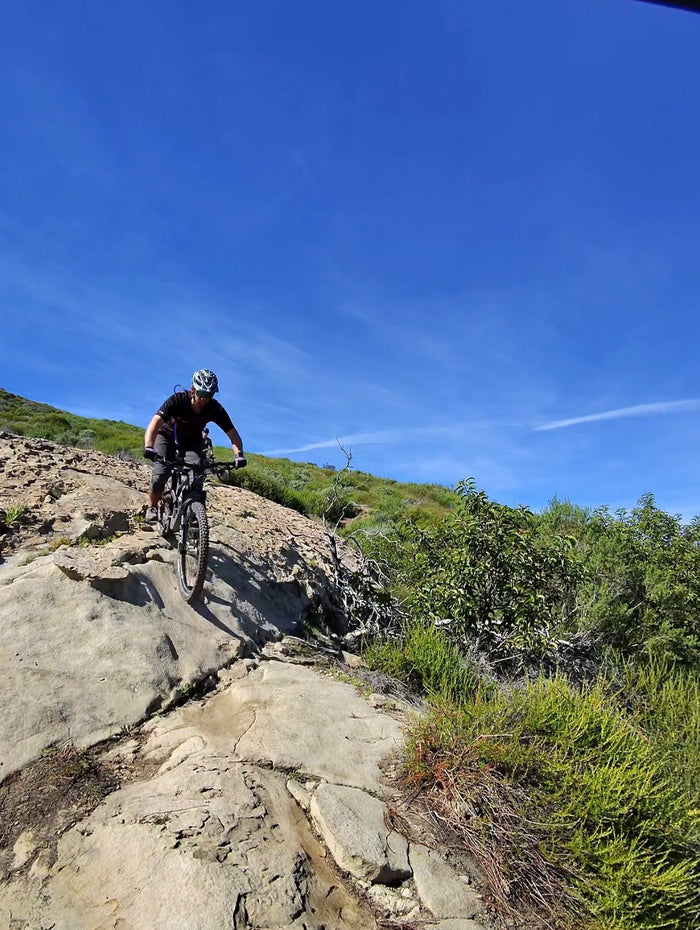 Mountain biker riding down a rocky trail under a blue sky