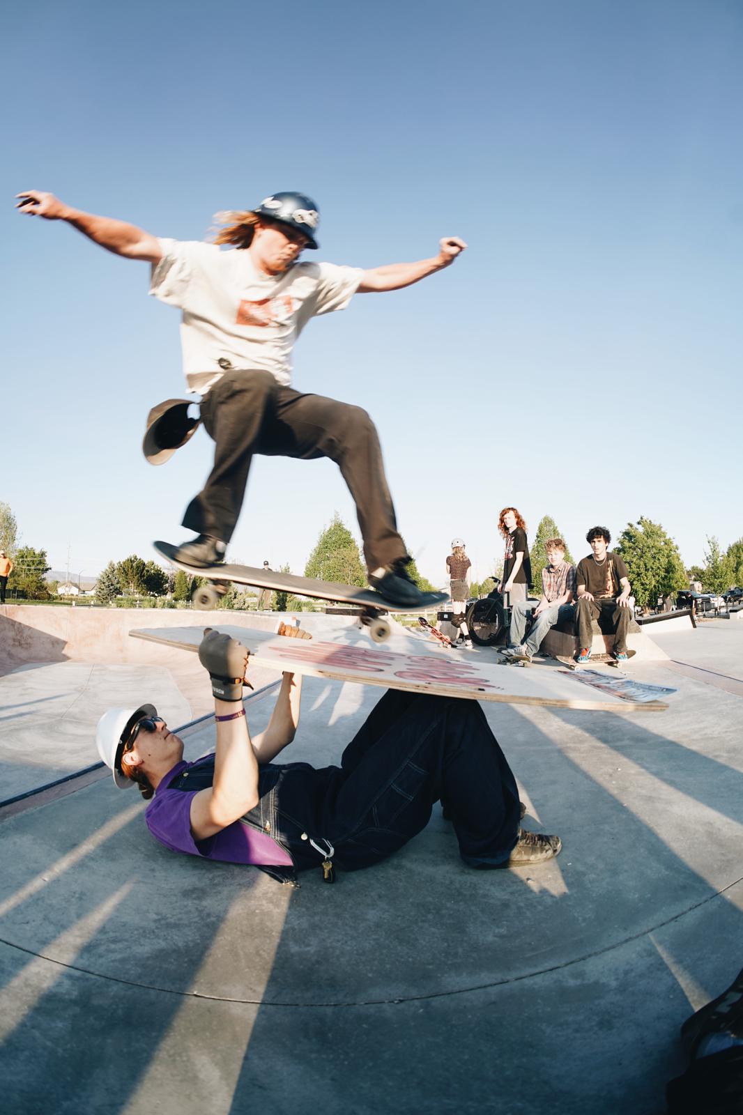 Skater ollieing over another rider at a skatepark